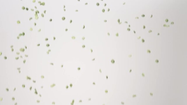 Dried raw Split Peas raining down on a white backdrop in slow motion close up macro.
