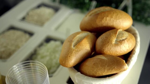 Fresh bread rolls arranged in basket on catering counter with buffet food background, dining setup and hospitality service atmosphere indoors