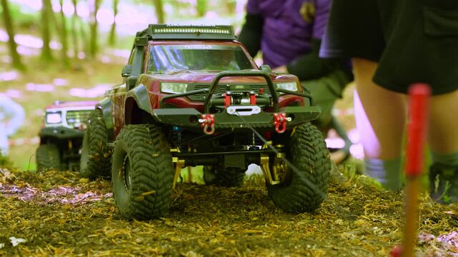 A low angle close-up shot of scale model RC crawler trucks navigating over a rough terrain course during an outdoor remote control car competition