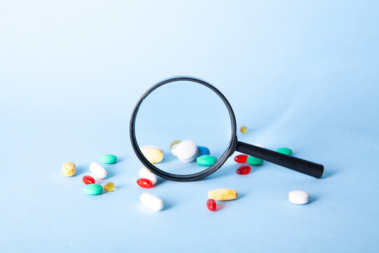Magnifying glass and colorful pills on blue background. Focus on magnifier