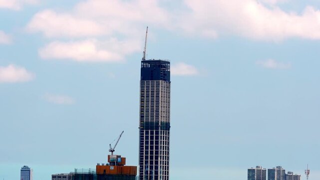 A timelapse video showing the construction progress of a tall skyscraper with cranes against a partly cloudy sky.