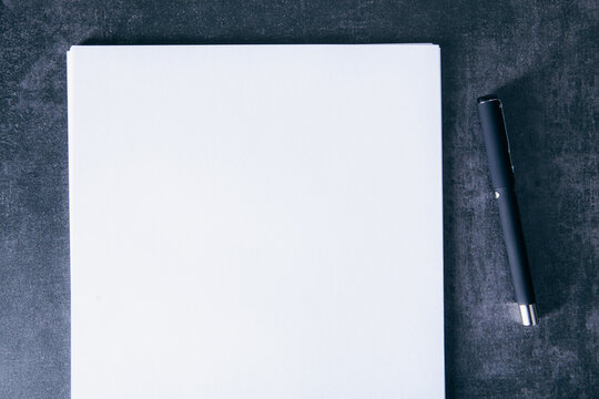 Blank white paper with pen on black background, top view.