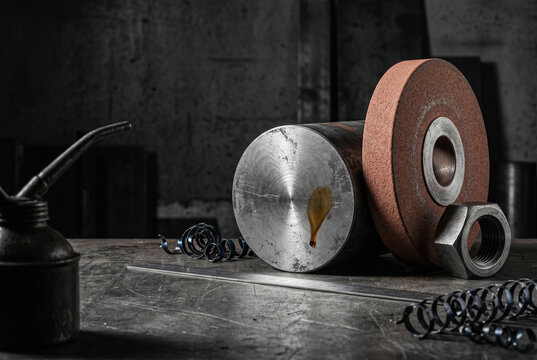 A monumental, close-up study of engineering precision, showcasing a cylindrical steel workpiece and a terracotta-brown vulcanite grinding wheel highlighted by a sharp amber oil smudge.
