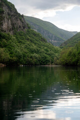 Fototapeta premium Canyon view in Matka with green trees and water reflecting clouds in North Macedonia.