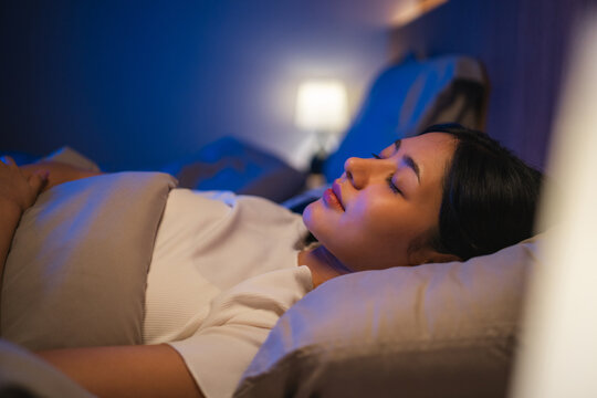 Beautiful asian woman lying in the bed at night. Young woman sleeping well in comfortable cozy fresh bed on soft pillow linen. Health and rest concept.