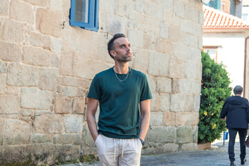 Fototapeta premium Handsome man casually walking through the city looking to the side, glancing at the houses