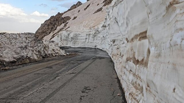 Spring mountain road carved between tall snow walls in Tette heights, showing melting layers and rugged slopes under a dramatic cloudy sky.
📍Tatte, Hawraman Takht, Kurdistan 