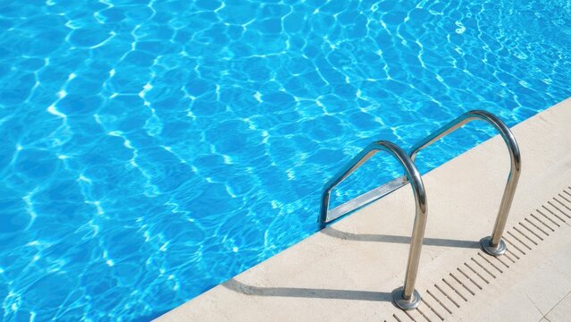 Sunlit blue swimming pool edge with stainless steel ladder and shimmering water reflections