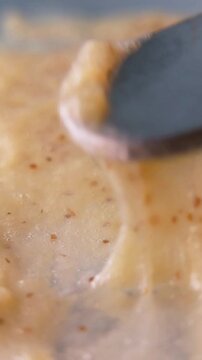 Close up of elastic texture of brown cream smear being lifted by a metal tool. Detailed cosmetic product consistency and texture shot.