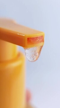 Closeup of transparent serum dispensing from orange pump nozzle. Vertical footage for fresh vitamin C beauty concept on white background.