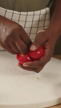 Vertical video: Placing red pepper on board, hands coring, rinsing, slicing for prep, checked apron