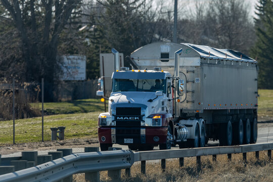 Quebec, Canada, 24 April 2026 : A Mack semi truck with a grain trailer drives on a rural highway under a clear sky.