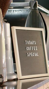 Vertical video: Panning camera framing board with TODAYS COFFEE SPECIAL on counter, showing roaster