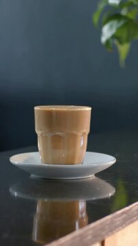 Vertical video: Shifting camera showing ridged glass on saucer at cafe with reflection and plant