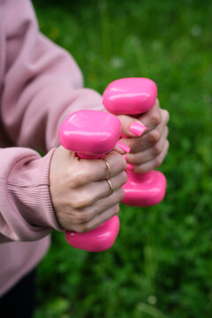Female hands with pink manicure holding pink dumbbells outdoors during fitness workout. women's fitness concept