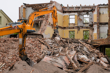Fototapeta premium Excavators demolishing abandoned brick building with massive rubble and debris at worksite