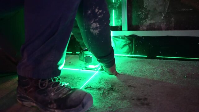 Construction worker using a green laser level on a floor