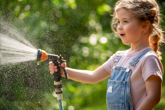 Happy 5 year old girl playing with a garden hose and water splashes on a sunny summer day, child&rsquo;s delight and outdoor fun.
