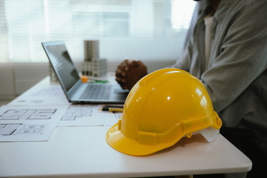 An architect or engineer works on a laptop with building plans and safety equipment, representing construction planning, project management, architecture, and engineering design.