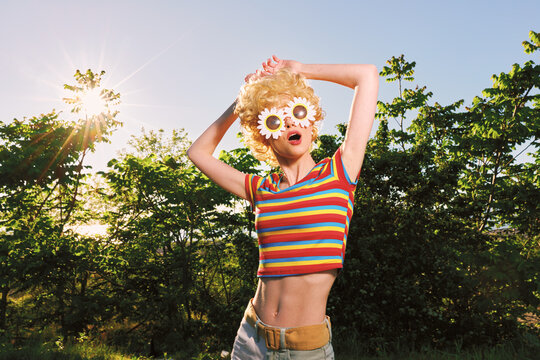 Energetic young woman dances outdoors in a striped crop top and flower sunglasses, sunlit joy and a breezy park vibe