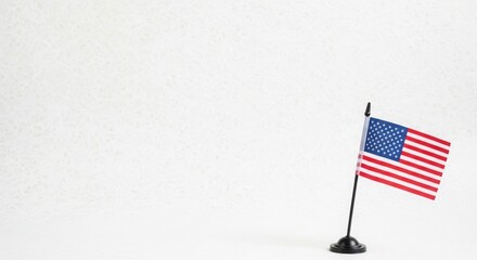 Fototapeta premium Small american flag on black stand against textured white backdrop, representing american values and freedom.