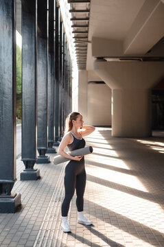 Woman in athletic wear holding a yoga mat outdoors near pillars