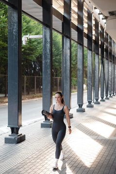 Woman in athletic wear walks with yoga mat outside modern building