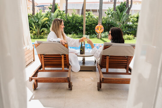 Two female friends cheers with champagne by a pool