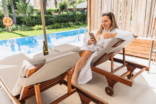 Woman in a bathrobe relaxing poolside with her phone