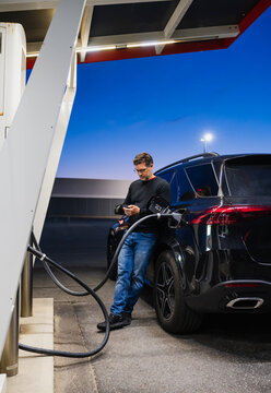 Man checks phone while his electric car charges at night