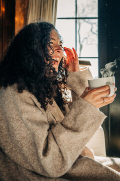 Smiling woman enjoying a hot drink by a sunlit window