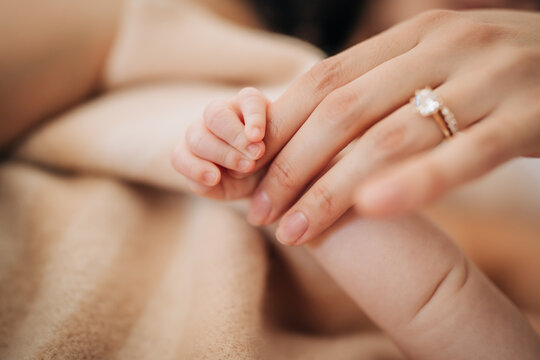 Mothers hand with wedding ring holding babys finger