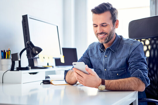 Smiling man using cell phone at desk in office