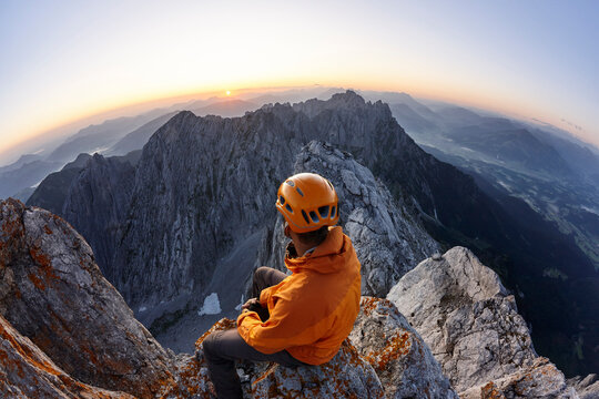 Climber with orange helmet sitting on Ellmauer Halt at sunrise, Wilder Kaiser, Ellmauer Halt, Tyrol, Austria