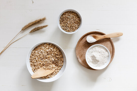 Rye ears and bowls of rye flakes, rye flour and rye grains on white background
