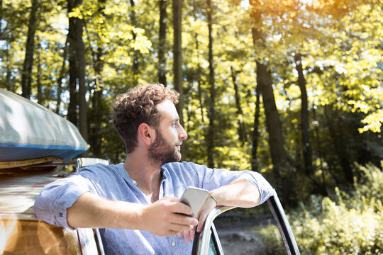Young man with cell phone at car in forest