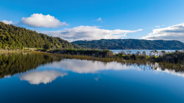 Clouds and blue sky reflected in the tranquil waters of Te Matahi Lagoon, which lies beside the larger Lake Rotoma in the Rotorua Lakes district, New Zealand
