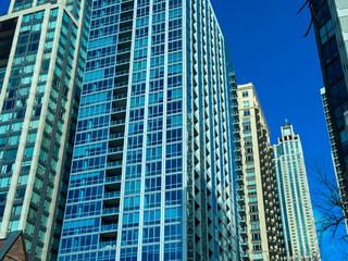 Obraz premium Modern buildings reach up to the blue sky in a bustling city on a clear day, showcasing urban architecture and city life from a low angle perspective with no people nearby