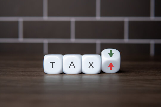 White blocks spelling the word TAX next to a tilted cube showing green down and red up arrows. Tax cuts, tax increases, financial planning, and government fiscal policy changes concept.