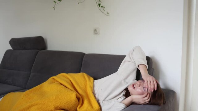 Young woman lies under a blanket suffering from rotavirus infection with fever headache weakness and stomach discomfort resting at home during acute illness and recovery period