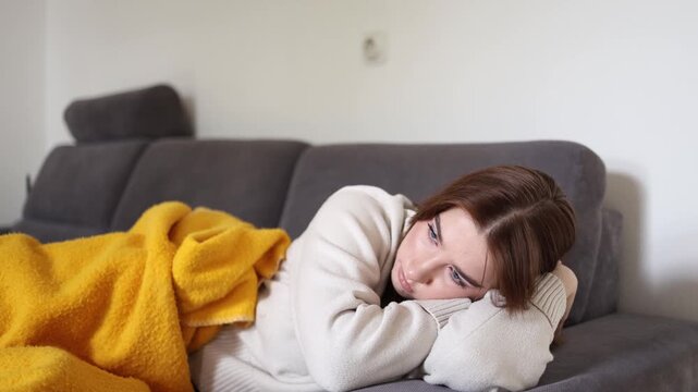 Young woman lying exhausted under warm blanket during gloomy autumn season feeling emotionally drained and physically tired while reflecting on life and coping with seasonal fatigue