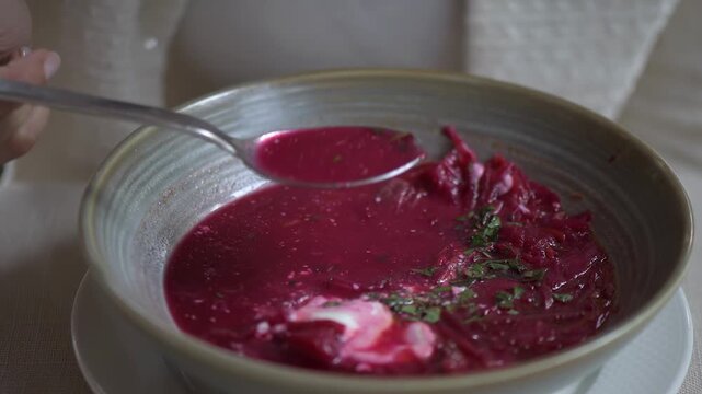 Woman eating traditional red beetroot soup with spoon in restaurant during lunch time.