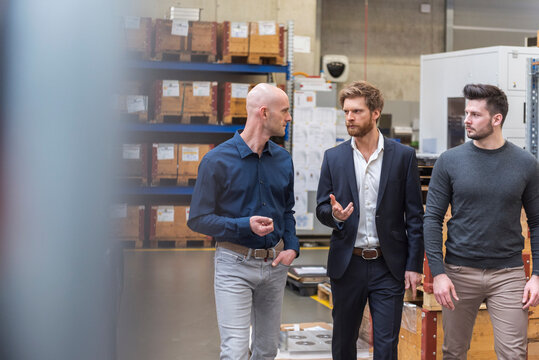 Three men walking and talking in factory storeroom