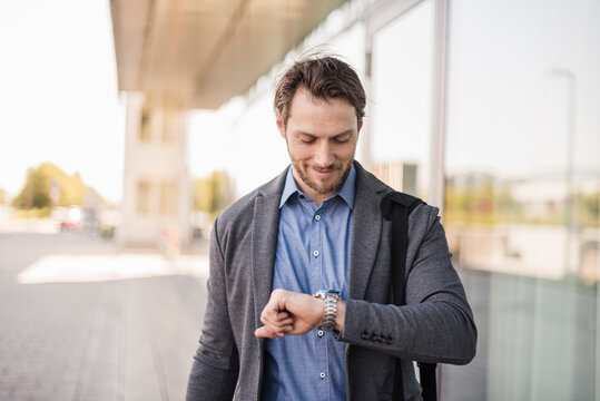 Smiling businessman with laptop bag checking the time