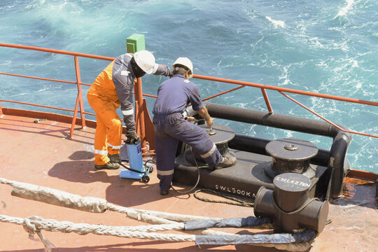 crew members performing maintenance work and greasing fairlead roller equipment on the poop deck of a cargo ship underway in open ocean