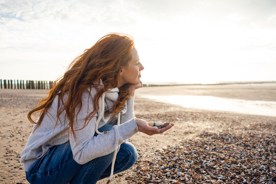 Redheaded woman collecting shell on the beach