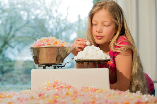 Girl behind scales, weighing sugar cubes and a lot of candies