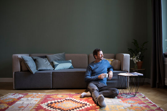 Man sitting on the floor in his living room looking through window