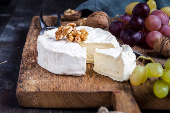 Wooden board with sliced camembert, walnuts and grapes