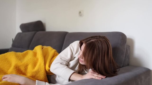 Young woman lying on sofa and struggling to breathe while experiencing severe throat swelling and respiratory symptoms during illness home healthcare concept with infection complications